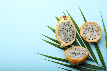 Delicious cut dragon fruits (pitahaya) and tropical leaf on light blue background, flat lay. Space...