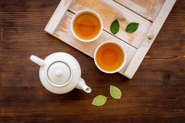 Black tea in cups with white teapot and green leaves