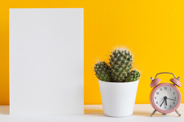 Mockup with paper blank, alarm clock, and cactus, or succulent against yellow wall with copy space for text. Place for text. Minimalism