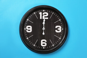 Stylish analog clock hanging on light blue wall