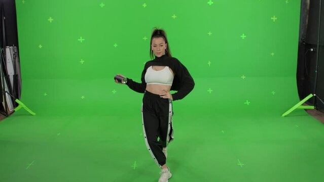 A young woman dancing on a green screen background. Attractive girl making content for social media. Female hooligan paints the camera with spray paint. Chroma key