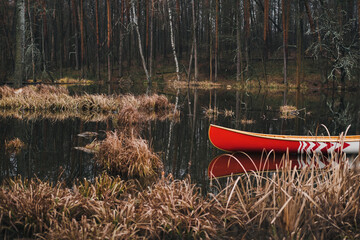 Beautiful forest lake and a canadian canoe. Red wooden boat floating on the pond, spring or autumn season