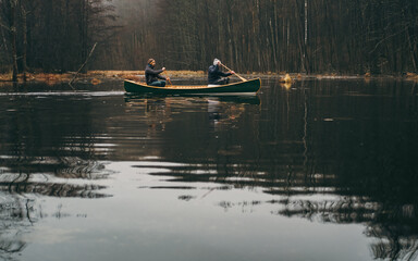 Two men paddling a green canoe on the forest lake. Active lifestyle, beautiful autumn or springtime forest scenery