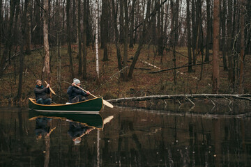Two men paddling a green canoe on the forest lake. Active lifestyle, beautiful autumn or springtime...