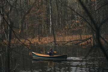 A person paddling a wooden canoe along the beautiful forest river. Tranquil autumn scene with a man in a boat