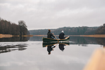 Two men paddling in a canadian canoe on the lake. Active lifestyle, a wooden boat on the surface of...