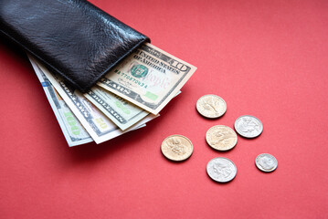 black leather wallet with dollar bills in different denominations and coins on a red background