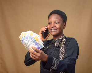 African Nigerian lady excited as she stares at the spread of multiple naira notes, cash, currency...