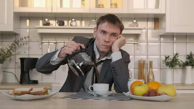 Tired Man Pouring Coffee Early in the Morning, Having Breakfast after Sleepless Night. Coffee Spills over the Rim of Cup. Business, Lifestyle, Overworking Concept