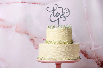 Beautiful wedding cake and topper with word LOVE on light background