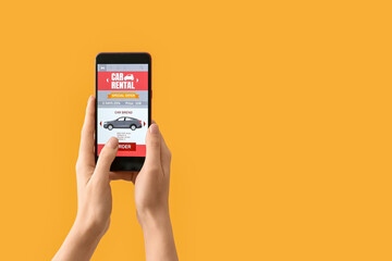 Female hands and mobile phone with open car rent app on yellow background