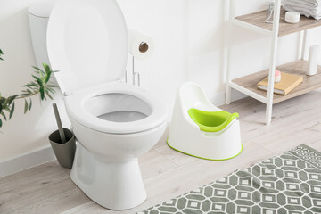 Toilet bowl, holder with paper rolls, potty and shelf unit with bath supplies near white wall