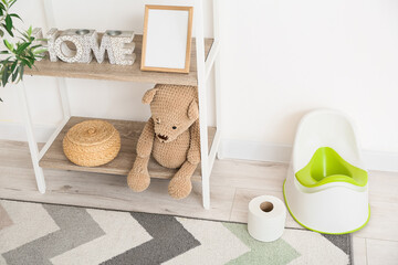 Shelf unit with toys, potty and toilet paper roll on floor near white wall
