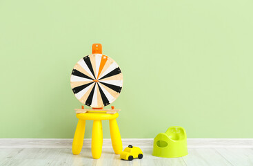Potty, toy car and table with wheel of fortune on grey wooden floor near color wall