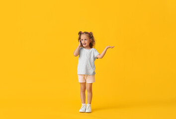 Adorable little girl talking by mobile phone on yellow background