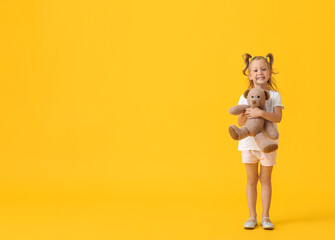 Adorable little girl with teddy bear on yellow background