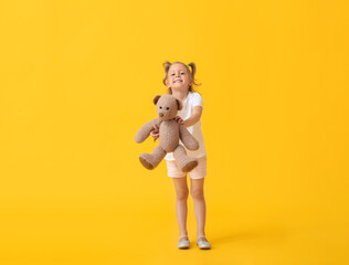 Adorable little girl with teddy bear on yellow background