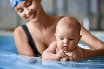 Adorable little baby with coach in swimming pool, closeup