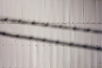電線の影が写るトタンの壁