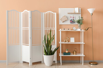 Interior of stylish room with pegboard, shelving unit and folding screen