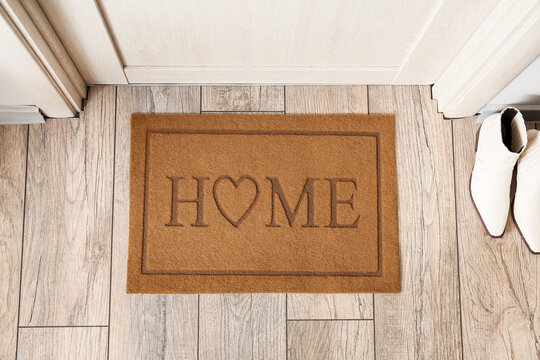 Stylish mat with word HOME near light wooden door in hallway