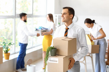 Young man holding boxes with things in office on moving day