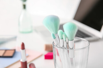 Glass with set of makeup brushes on table, closeup