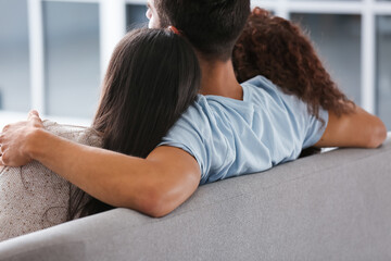 Man and two beautiful women sitting on sofa. Polyamory concept