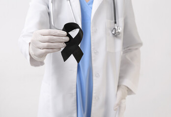 Doctor with black ribbon on light background. Melanoma concept