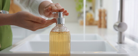Woman applying liquid soap on hand indoors, closeup. Banner design