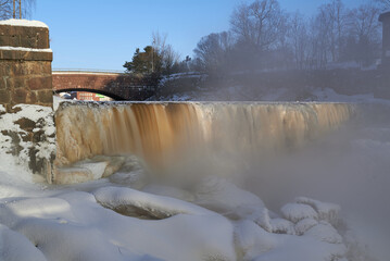 Water pours over frozen museum dam in the mouth of Vantaa River at the Vanhankaupunginkoski rapids (Vanhankaupunginkosken putous) on extremely cold winter morning in February 2021.