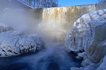 Water pours over frozen museum dam in the mouth of Vantaa River at the Vanhankaupunginkoski rapids (Vanhankaupunginkosken putous) on extremely cold winter morning in February 2021.