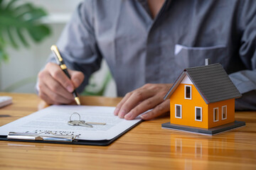 Real estate agent working sign agreement document contract for home loan insurance approving purchases for a client with house model and key on the table, concept of a contract to buy and sell a house