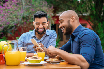 happy gay couple sharing screen of mobile phone and watching video outside in the garden