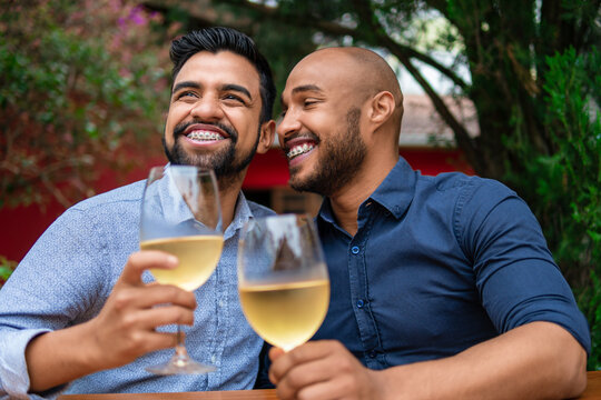 Romantic Gay Couple Smiling And Drinking Wine In Table Outside