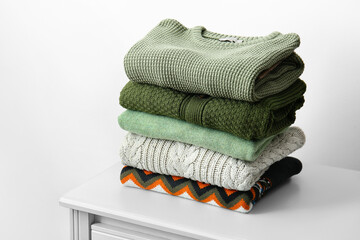 Stack of different stylish sweaters on table near light wall