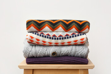Stack of stylish sweaters on wooden stool against light background