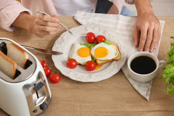 Young man eating tasty toasts with eggs, tomatoes and avocado in kitchen