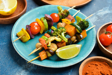 Plate with tasty vegetable skewers and spices on blue background, closeup