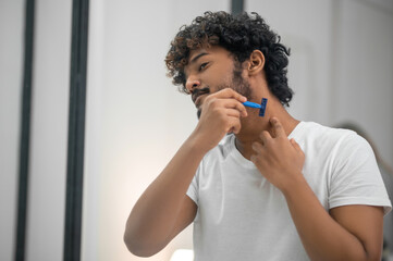 Fototapeta na wymiar Concentrated young man shaving himself before the mirror