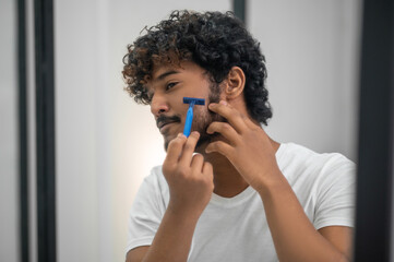 Focused guy using his safety razor for facial hair removal