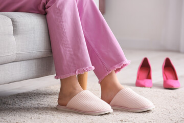 Young woman resting at home after changing high heels for soft slippers - obrazy, fototapety, plakaty