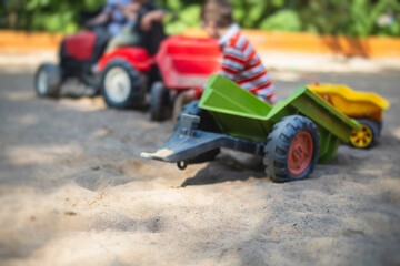 Fototapeta na wymiar Children playing in the sandbox sandpit, kids with toy car vehicle, playground in kindergarten day care