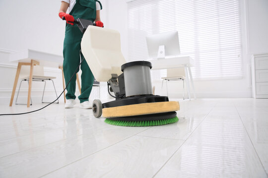 Professional janitor cleaning parquet floor with polishing machine in office, closeup