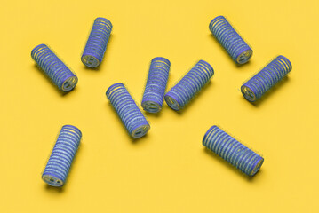 Fototapeta premium Blue hair rollers scattered on yellow background for hair styling and beauty salon concepts, these classic hair tools are used for creating curls and volume, essential for personal grooming and salon
