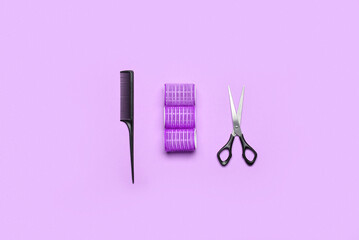 Hair curlers, brush and scissors on color background