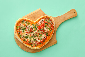 Wooden board with tasty heart-shaped pizza on green background. Valentine's Day celebration