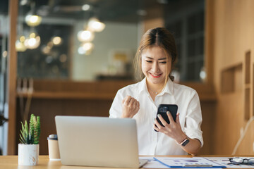 Excited young woman sitting at table with laptop and celebrating success