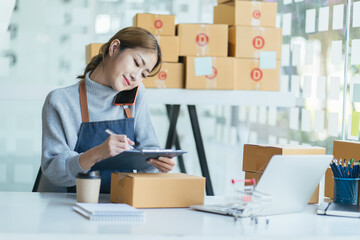 Happy young asian woman startup small business freelance holding parcel box and computer laptop and sitting on chair, Online marketing packing box delivery concept