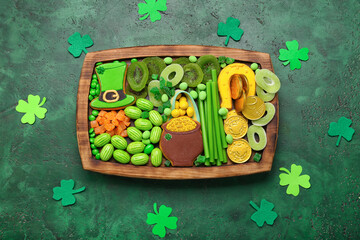 Wooden board with different sweets for St. Patrick's Day celebration on green background